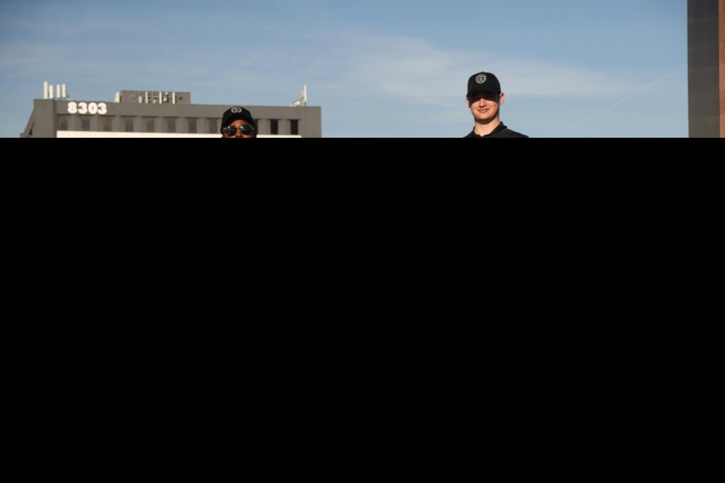 Two security officers in uniforms posing by a marked patrol vehicle outdoors.